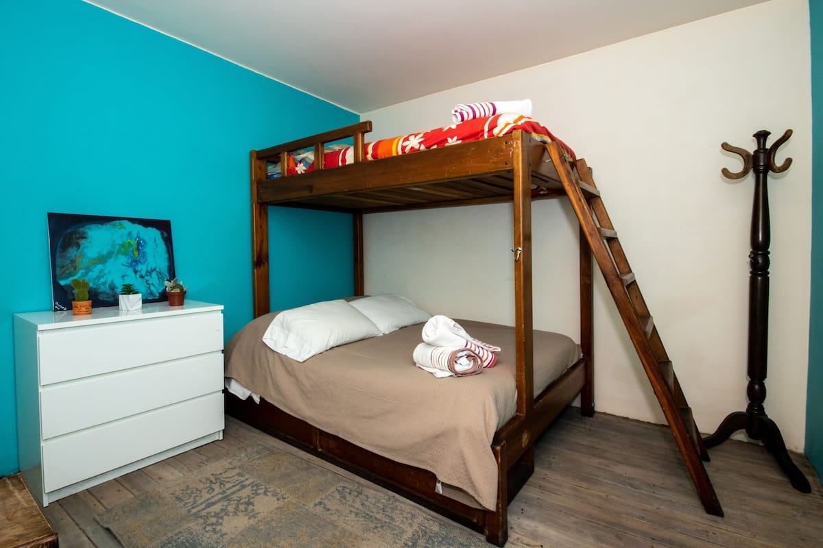 A bunk bed with a wooden frame, a white dresser with a painting, and a wooden floor.