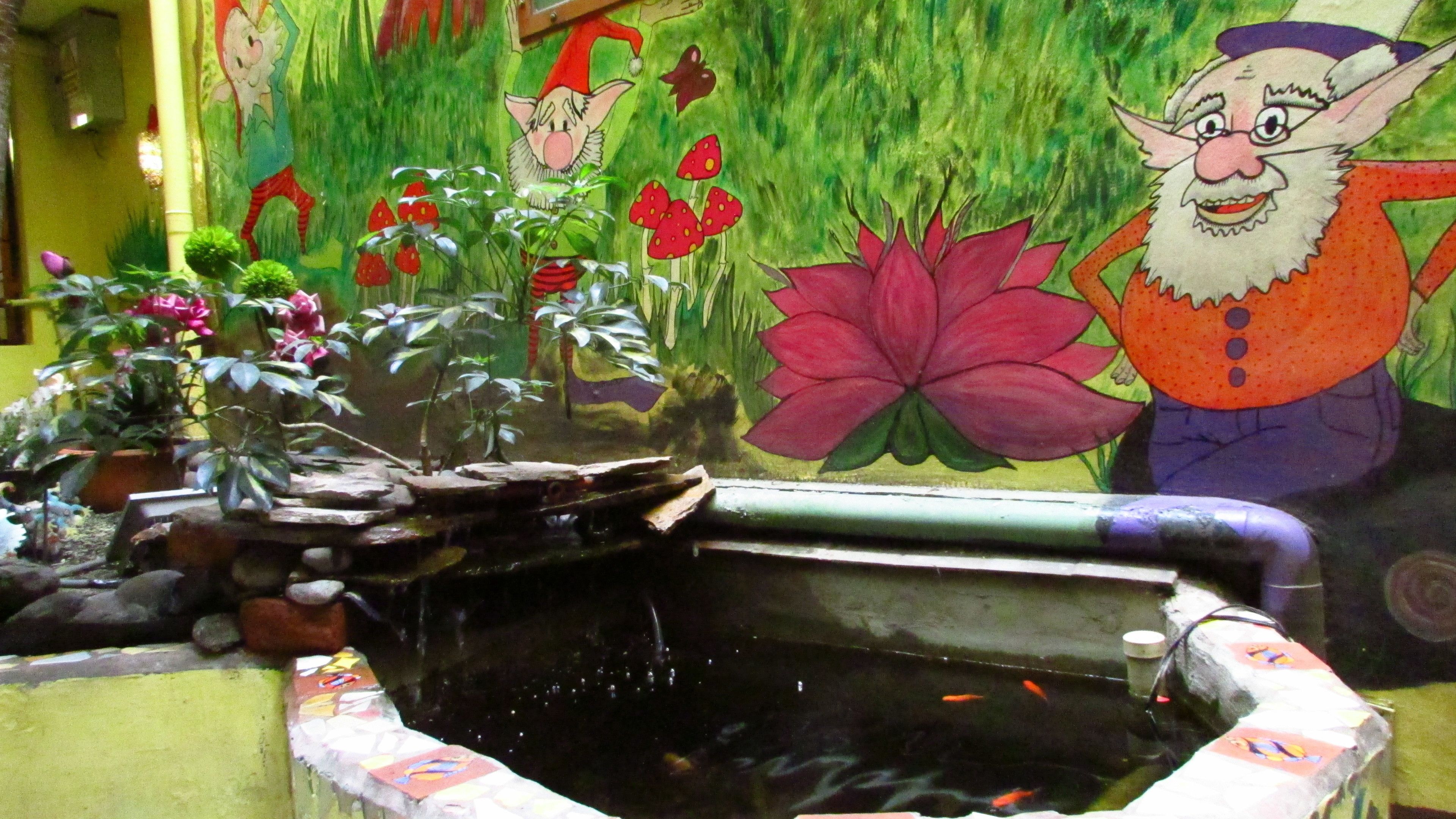 A decorative indoor pond with water plants and a mural of gnomes and flowers in the background.