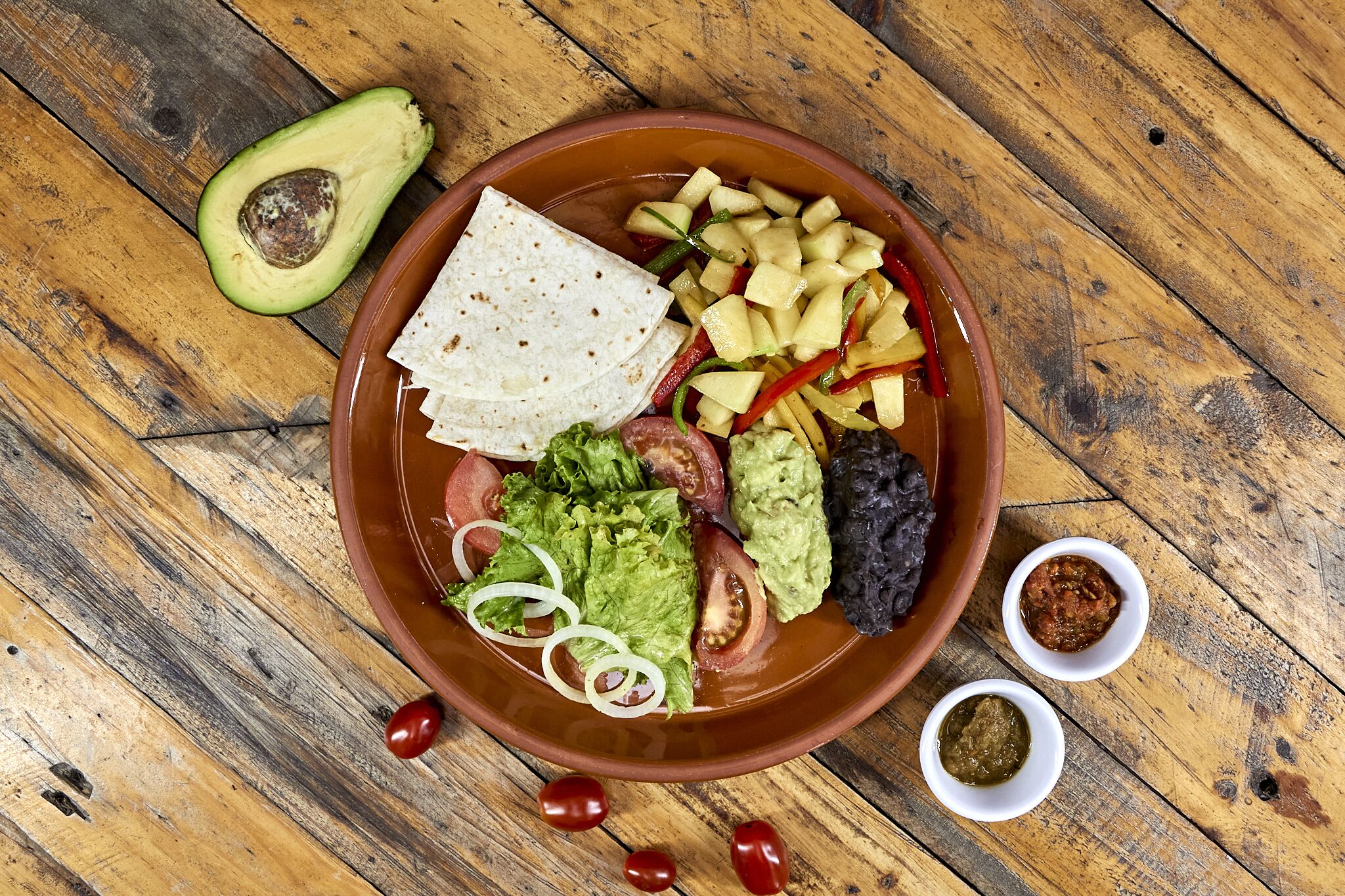 Un tazón de comida con tortillas, aguacate, tomates y pimientos sobre una mesa de madera.