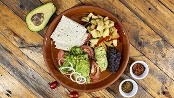 Un tazón de comida con tortillas, aguacate, tomates y pimientos sobre una mesa de madera.