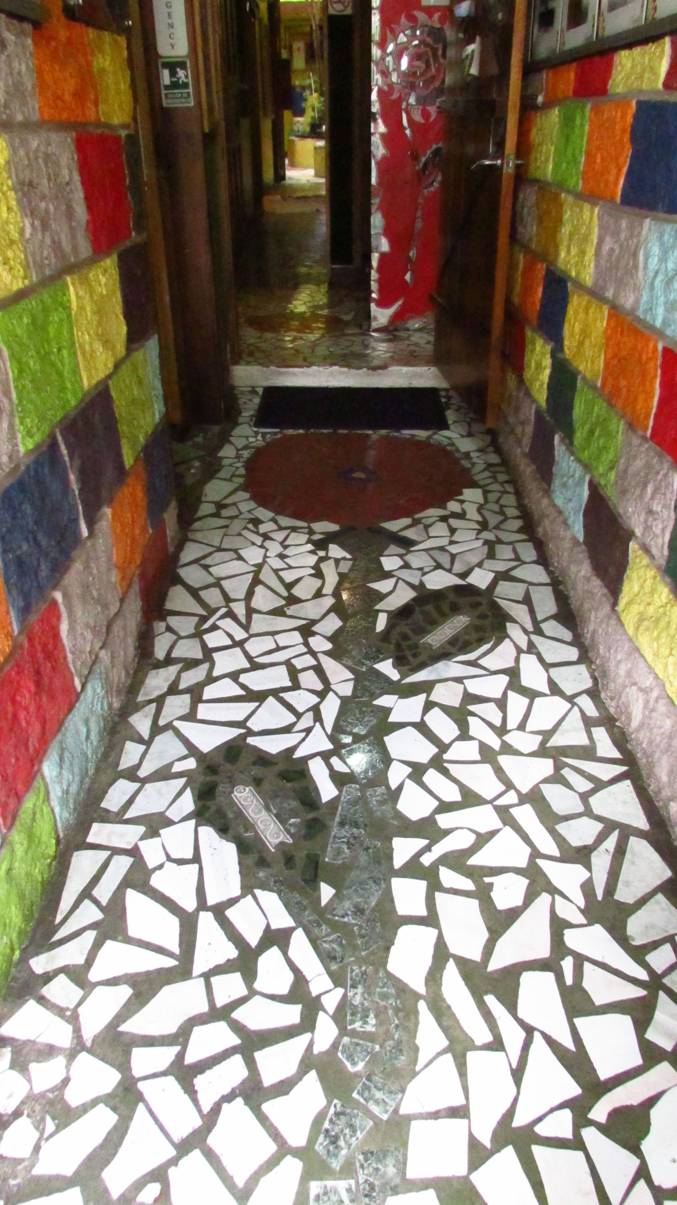 A narrow hallway with colorful mosaic walls and a floor of white and green tiles.