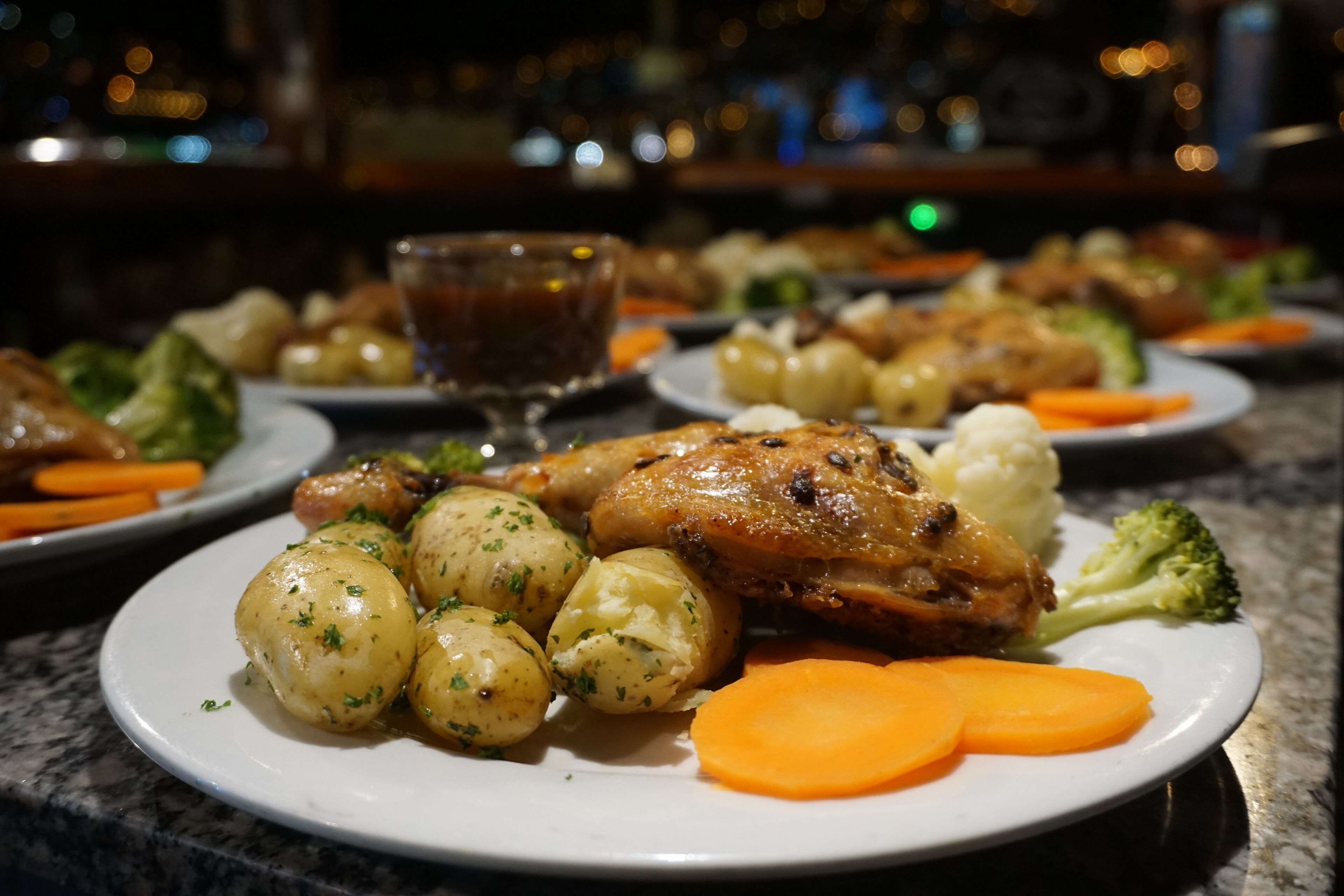 A dining table with plates of food, including roasted chicken, potatoes, and carrots.