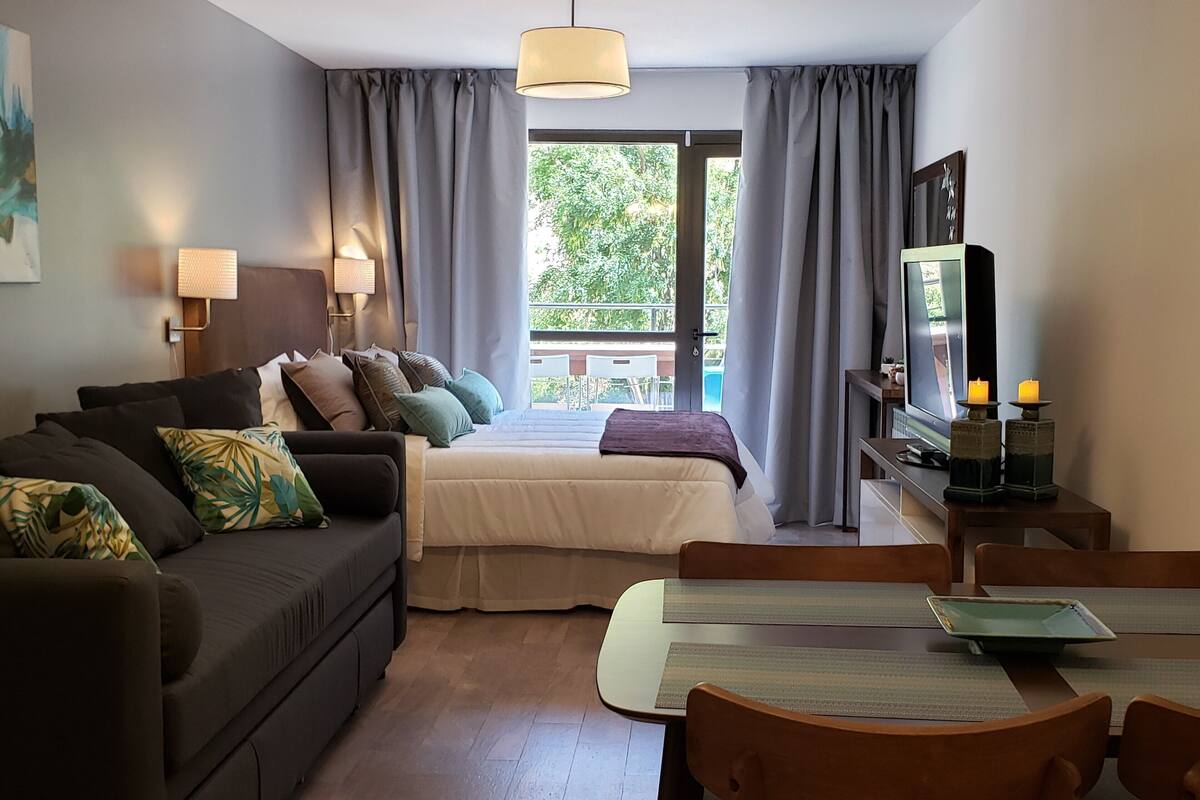 Moderni hotellihuone, jossa on sohva, sänky, ruokapöytä ja televisio.