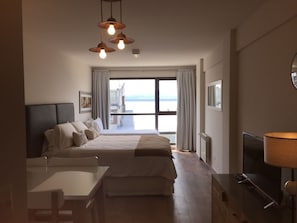 A hotel room with a bed, a desk, a TV, and a view of the sea. - Urbana Suites & Studios 440 (San Carlos de Bariloche)
