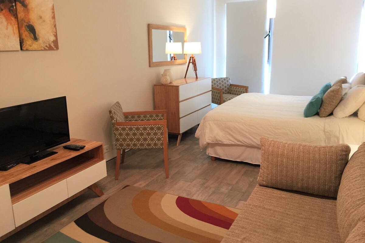 Hotellihuone, jossa on sänky, televisio, työpöytä, tuoli ja sohva.