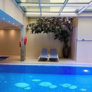 An indoor pool area with two striped lounge chairs, a large potted plant, and a glass ceiling. - Mandarin Al Shamal Hotel Apartments (Riyadh)
