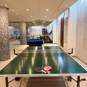 A ping pong table with paddles and balls, a treadmill, and exercise equipment in a well-lit room with a tiled floor. - Mandarin Al Shamal Hotel Apartments (Riyadh)
