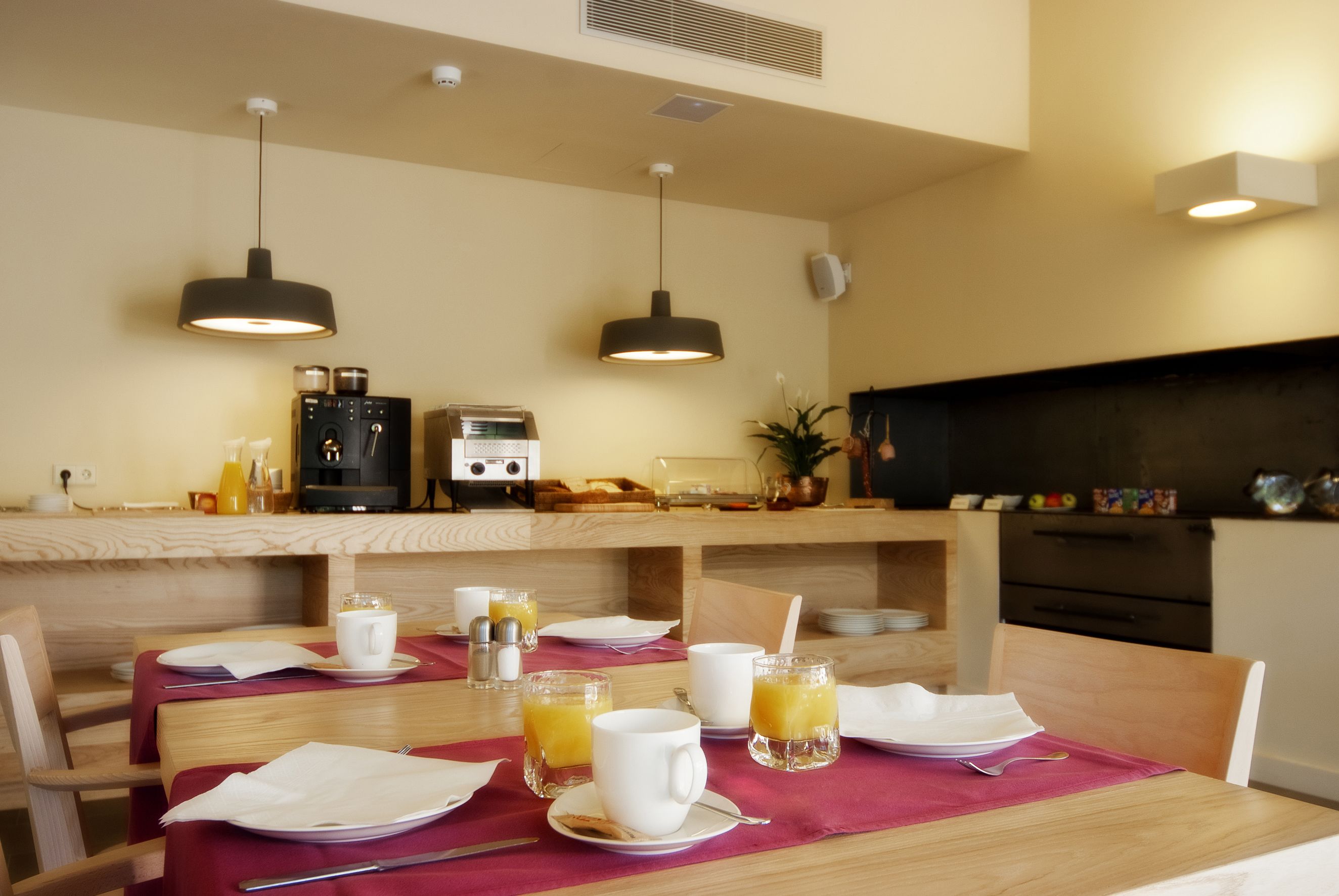 Una escena de desayuno con una mesa de madera, sillas y una encimera con electrodomésticos de cocina.