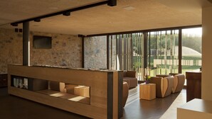A modern reception area with a wooden reception desk, comfortable seating, and large windows offering a view of the outdoors. - Hotel Restaurant el Molí (Pont de Molins)
