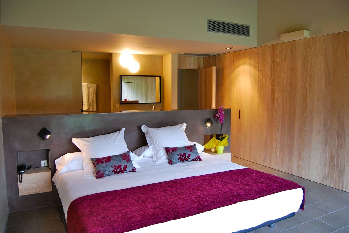 Un dormitorio moderno con una cama grande, una mesita de noche, un armario de madera y un espejo.
