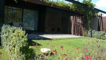 Un edificio moderno con grandes ventanales, un patio cubierto y un jardín bien cuidado con diversas plantas y flores.