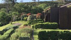 A landscaped garden with manicured hedges, flowering plants, and a modern building with a dark facade. - Hotel Restaurant el Molí (Pont de Molins)