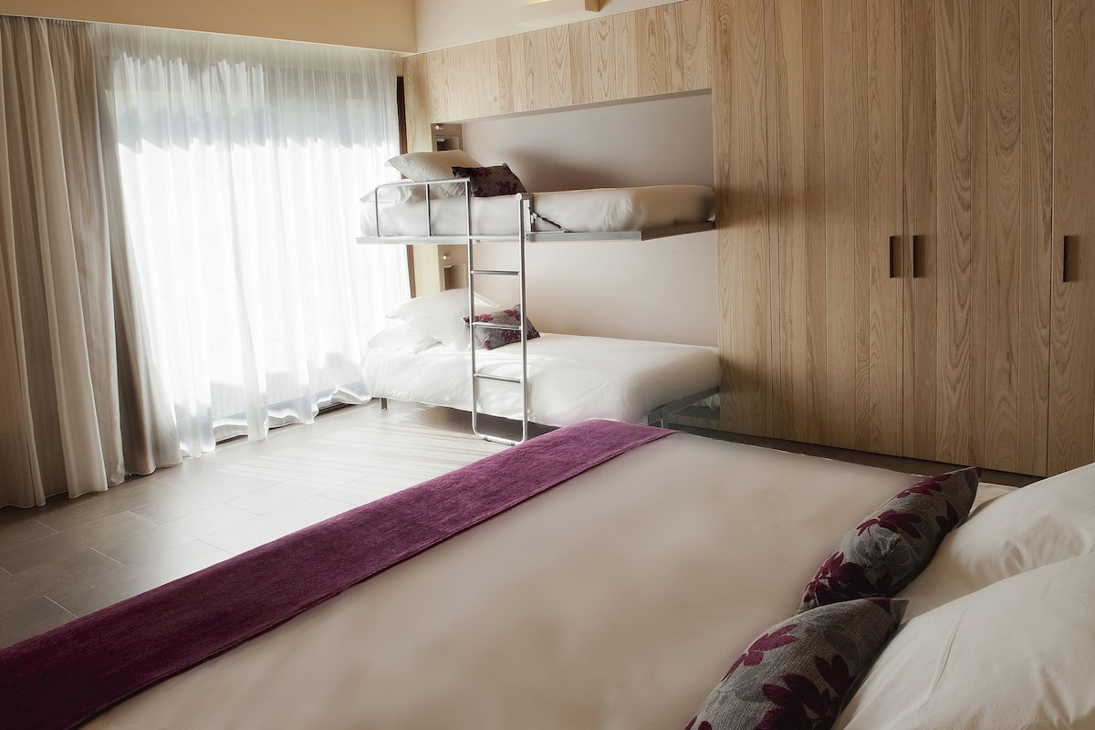 Habitación de hotel con una cama litera, una manta morada y paneles de madera en las paredes.