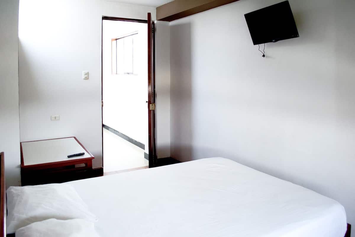 A hotel room with a bed, a small table with a remote control, a television mounted on the wall, and a door leading to a balcony.
