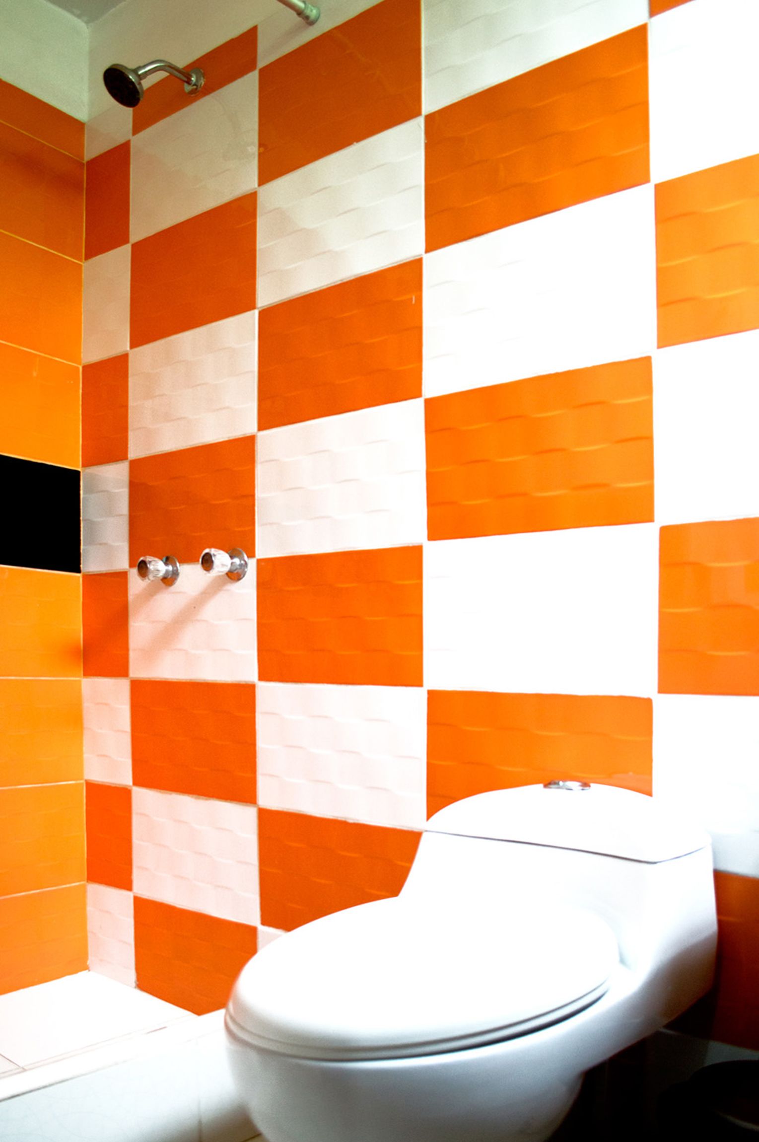 Un baño con baldosas anaranjadas y blancas a cuadros, un inodoro blanco y un cabezal de ducha.