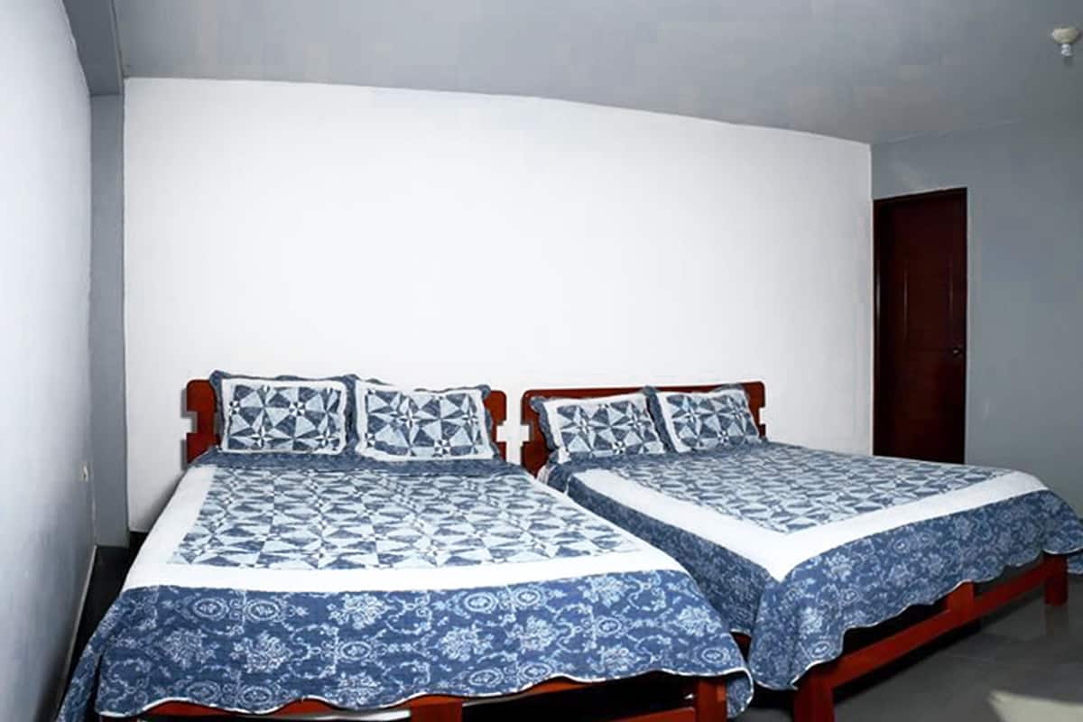 A room with two beds, each with a patterned bedspread and pillows, a wooden headboard, a dark door, and a flat-screen TV mounted on the wall.