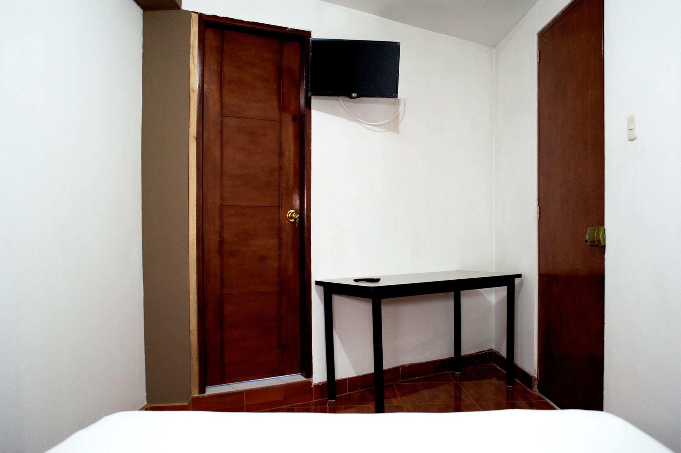 Ein Zimmer mit Holztür, einem kleinen Tisch und einem an der Wand befestigten Fernseher.