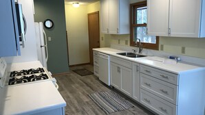 A kitchen with white cabinets, a stove, a sink, and a window.