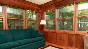 A cozy room with a green sofa, wooden walls, large windows, and a red rug.