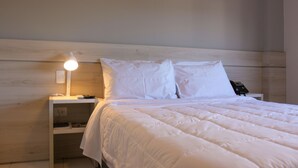 En pænt redt seng med hvidt sengetøj og puder, en sengetlamps og en telefon på natbordet.