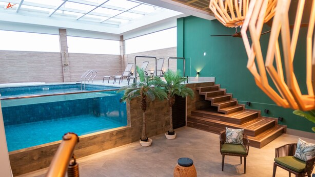 En indendørs swimmingpool med et glasloft, trætrin og siddeområder med hynder.