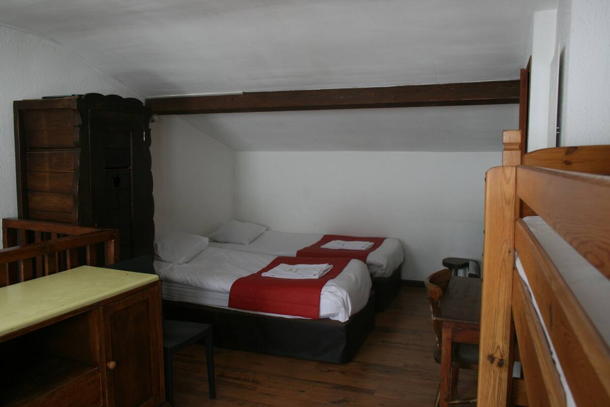 Une petite pièce, de taille modeste, comprenant deux lits simples, un bureau en bois et une chaise.
