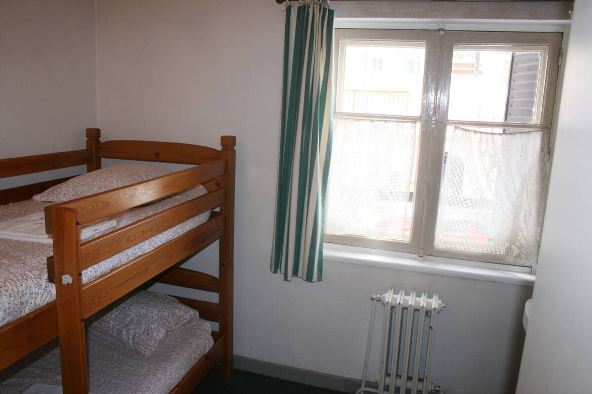Une chambre avec un lit superposé, une fenêtre avec des rideaux et un radiateur.