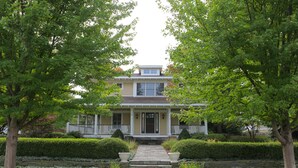 A two-story house with a front porch, a central entrance, and a small front yard with hedges and a pathway leading to the door. - Douglas Manor (Douglas)