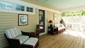 A covered porch with wooden flooring, a striped chair, a sofa with patterned cushions, and two framed artworks on the walls. - Douglas Manor (Douglas)