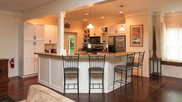 A modern kitchen with a central island, bar stools, white cabinetry, and a large window with curtains. - Douglas Manor (Douglas)