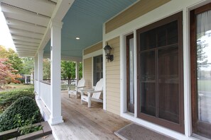 A covered porch with two white Adirondack chairs, a small table, and a large sliding glass door.