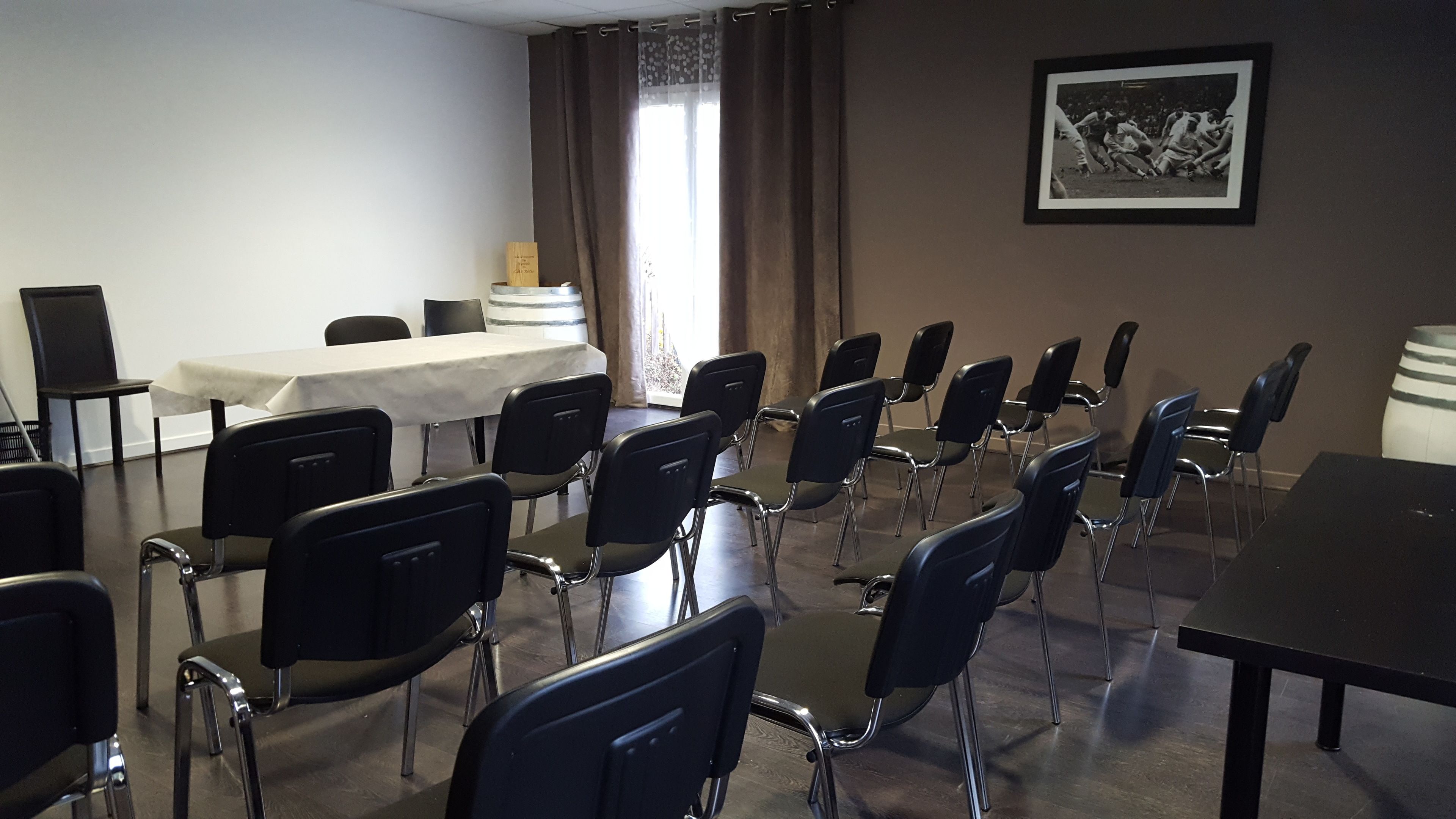 Un salón de conferencias con filas de sillas negras, una mesa con mantel blanco y una fotografía blanco y negro enmarcada en la pared.