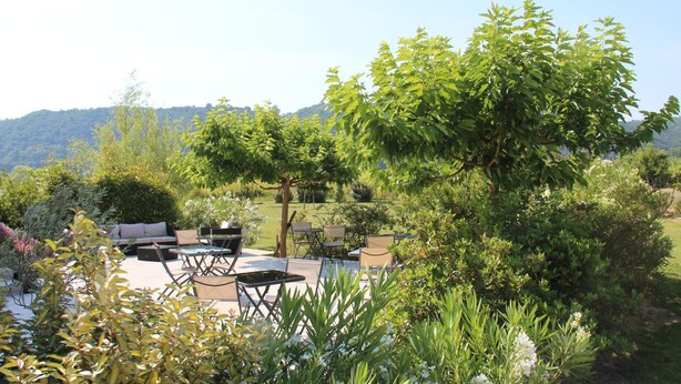 Une terrasse extérieure avec des sièges et une table, entourée de verdure et avec des collines en arrière-plan.