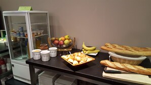 Un buffet de petit-déjeuner comprenant du pain, des viennoiseries, des fruits et des condiments.