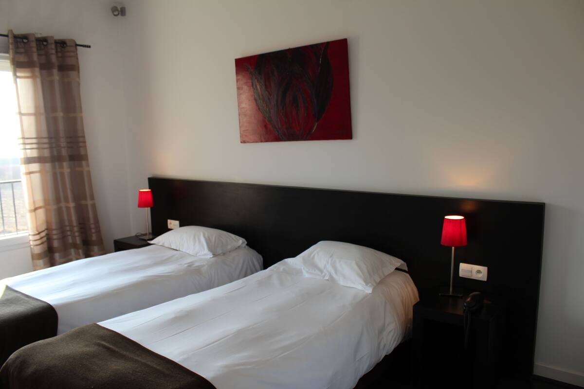 A hotel room with two single beds, a red lamp on each nightstand, and a red abstract painting on the wall.