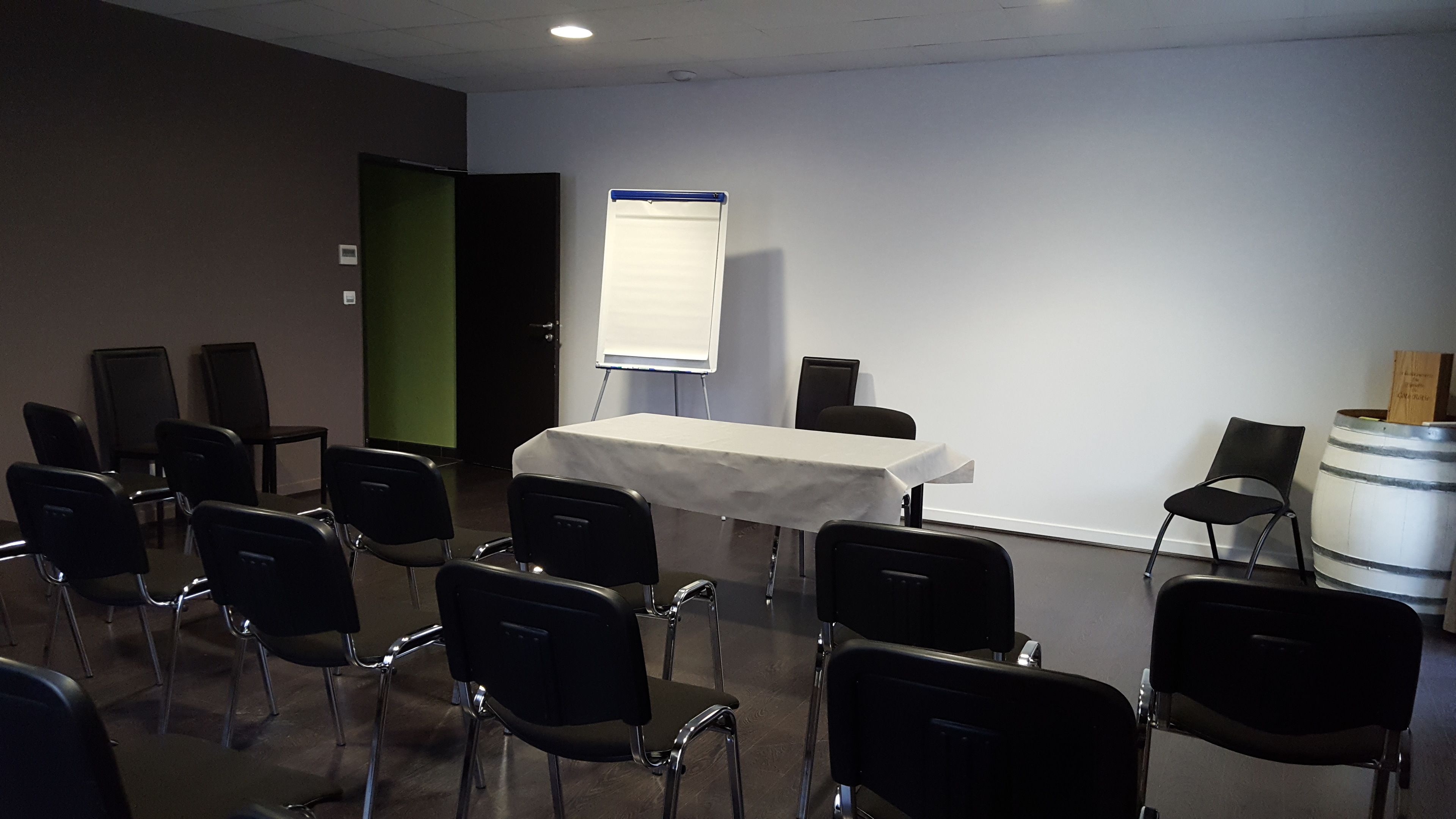 Une salle de conférence avec une table blanche, des chaises noires, un tableau blanc et un projecteur.