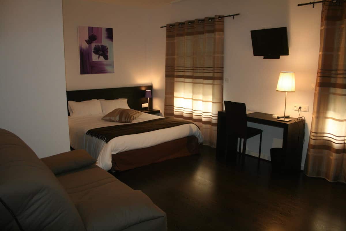 A hotel room with a bed, a desk, a chair, a TV, and a window with curtains.