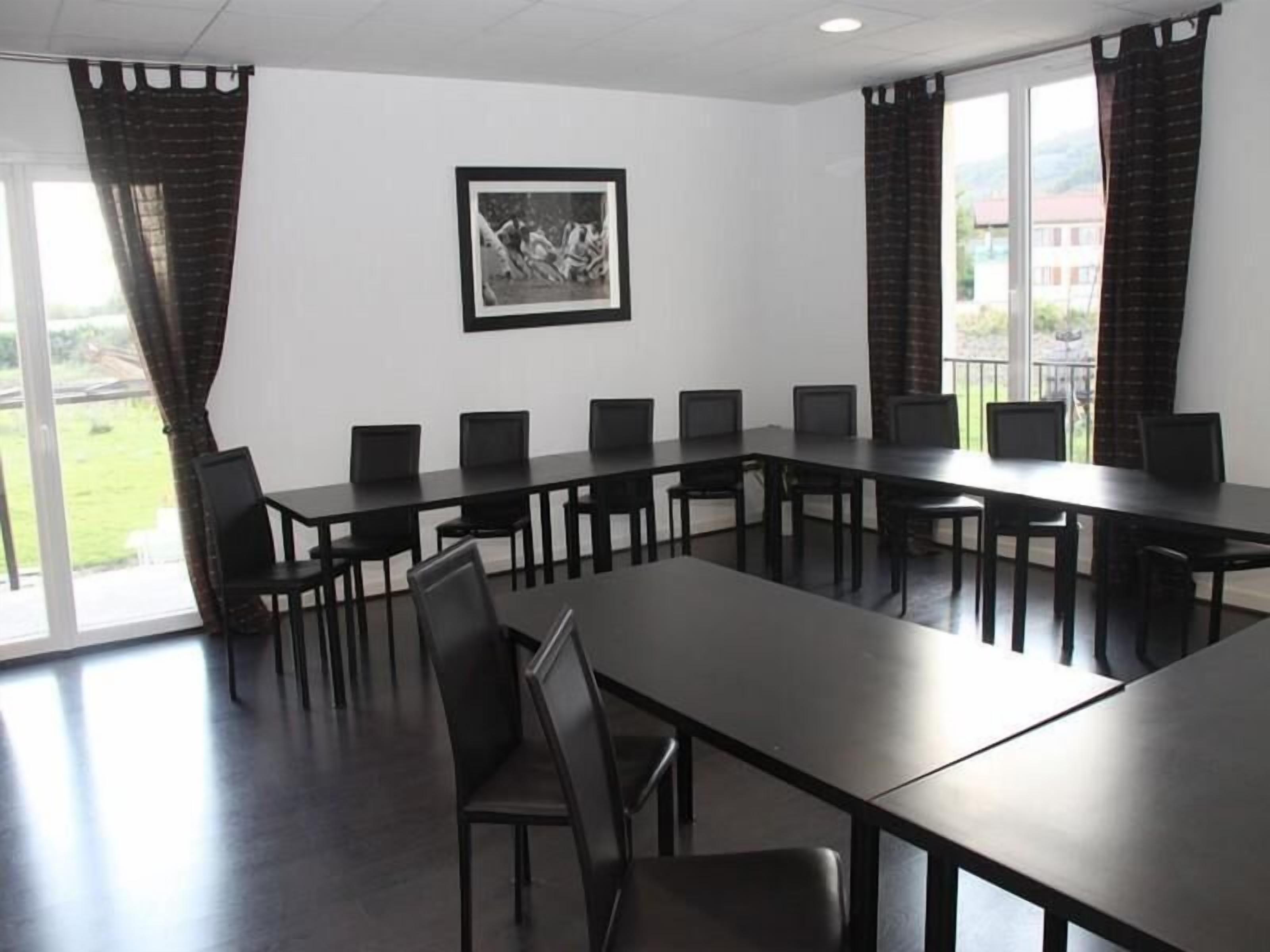 Un salón de conferencias con una larga mesa y sillas, ventanas grandes y un cuadro en la pared.