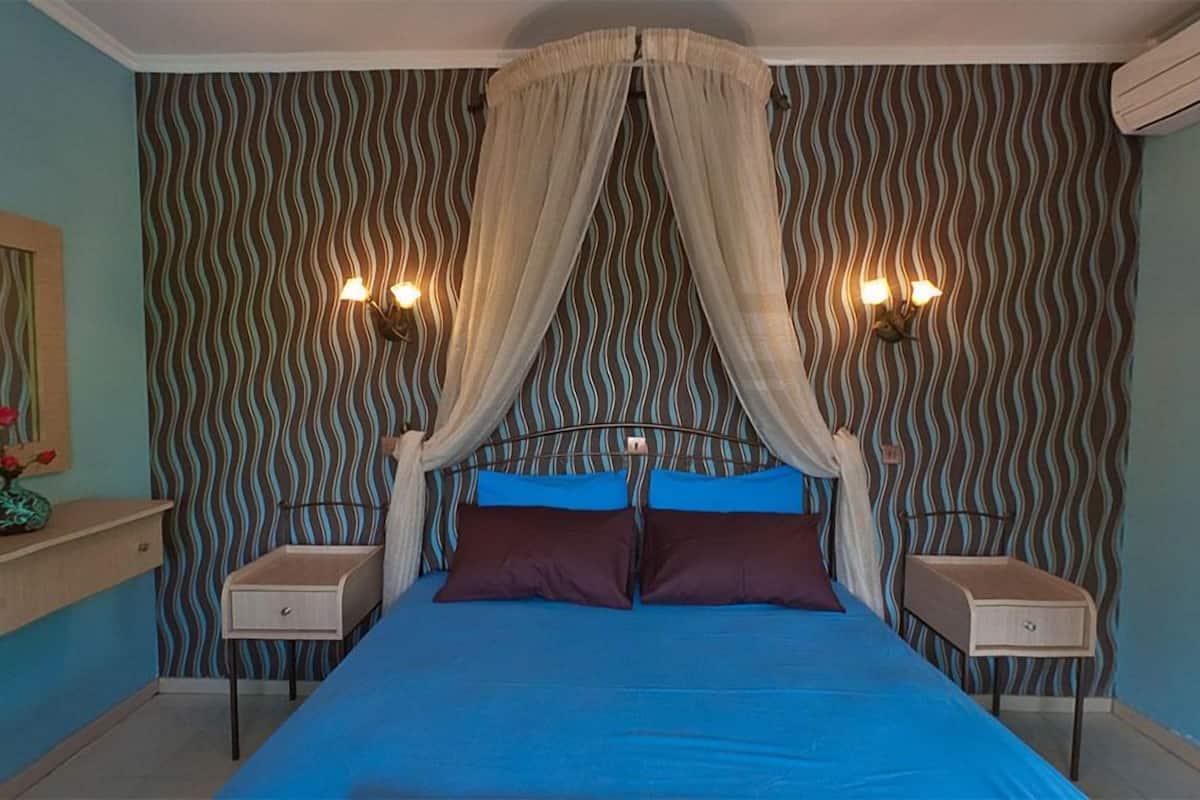 A bedroom with a canopy bed, two bedside tables, a nightstand, a mirror, and a vase with flowers.