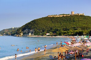 A beach with umbrellas and people, a castle on a hill, and a clear sky. - Ktima Garas (Dio-Olympos)