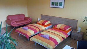 Hotellihuone, jossa on kaksi sänkyä, punainen nojatuoli, yöpöytä lampun kanssa ja seinällä oleva kehystetty kuva.