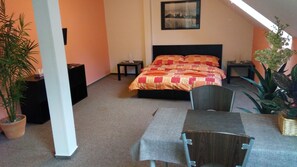 A bedroom with a bed, nightstands, a table, chairs, and potted plants. - Penzion Exotic (Ostrava)