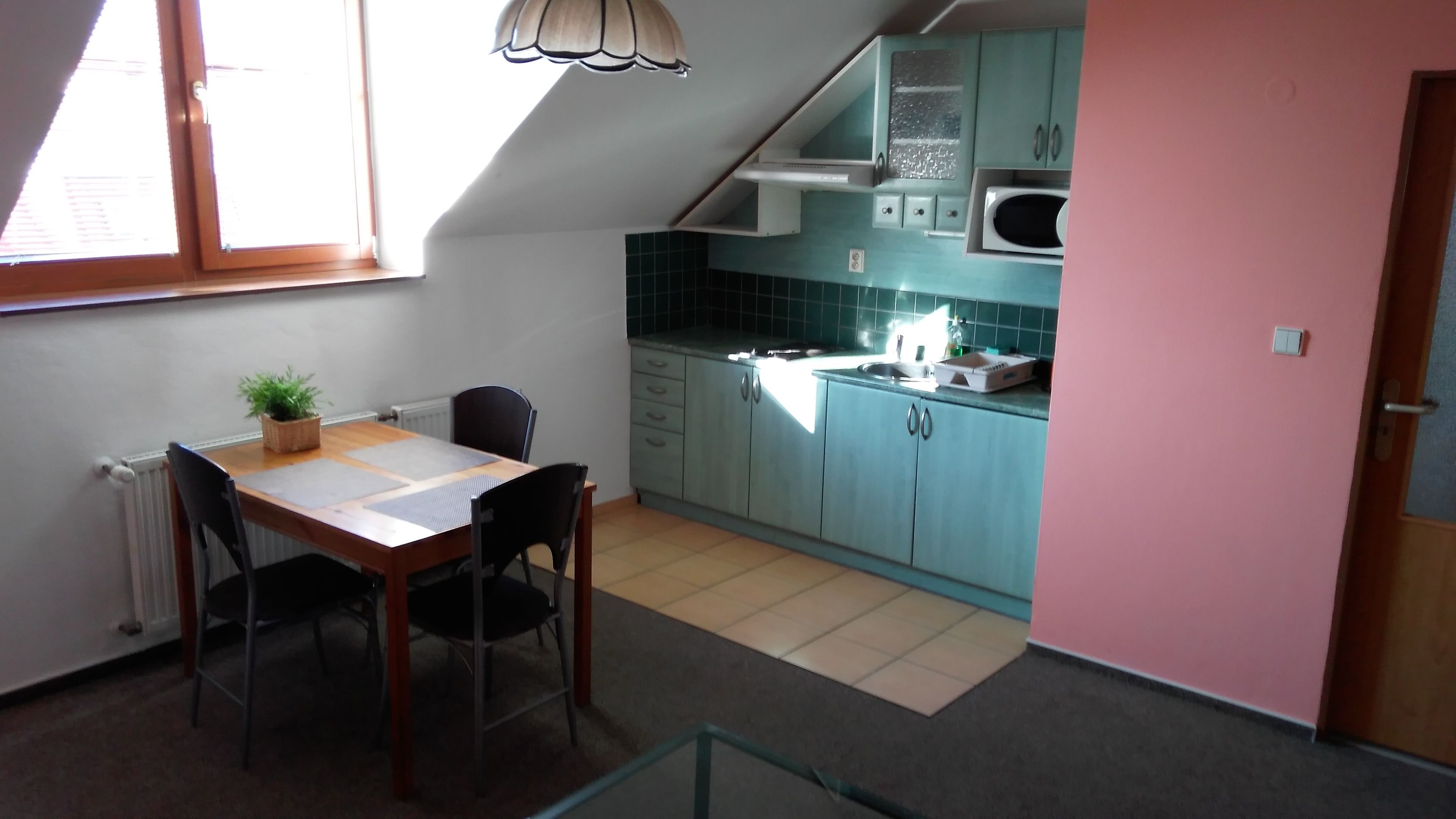 Een compacte keuken met blauwgroene kastjes, een magnetron en een eethoek met een tafel en stoelen.