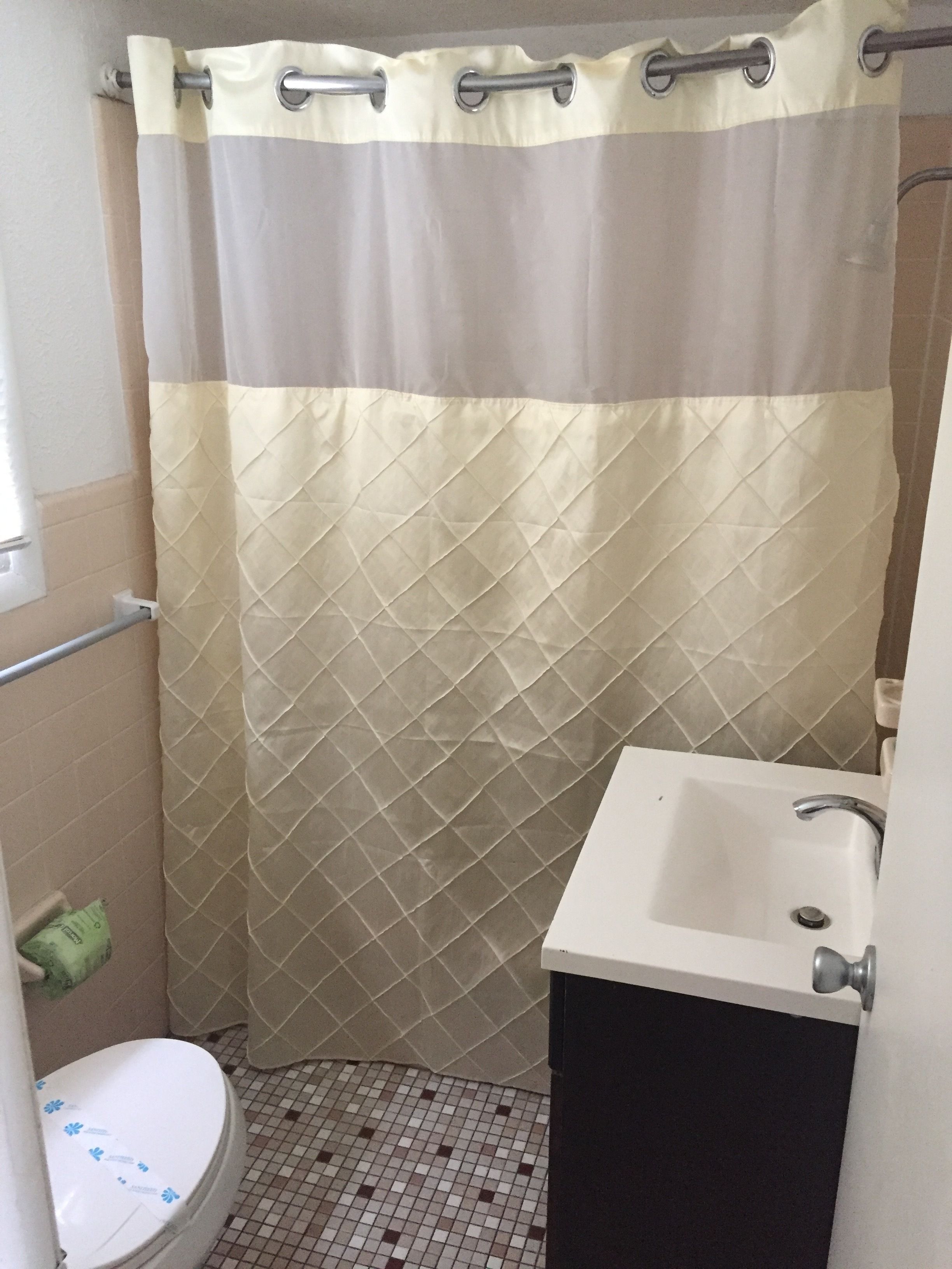 A bathroom with a shower curtain, a toilet, a sink, and a tiled floor.