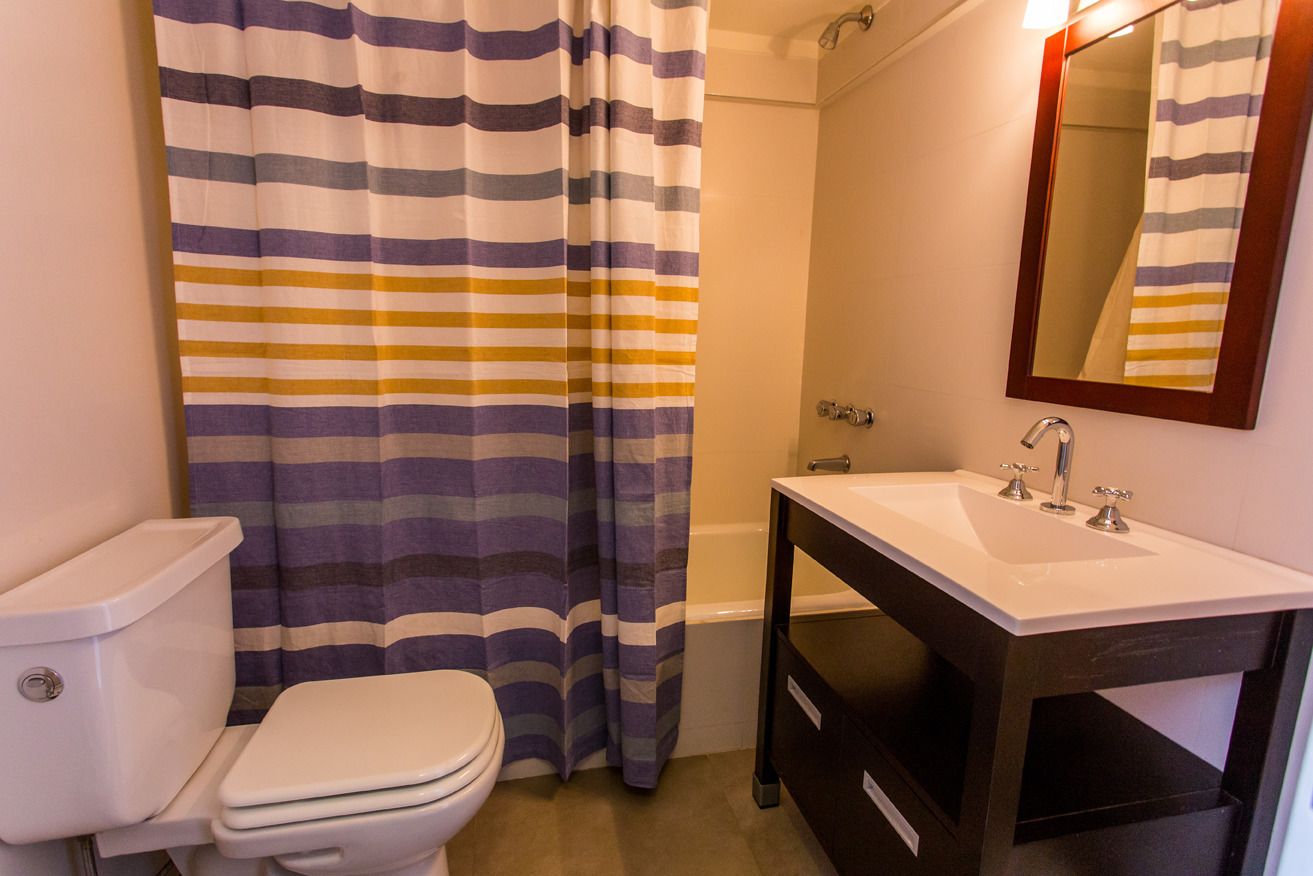 A bathroom with a striped shower curtain, a toilet, a sink with a mirror, and a bathtub.