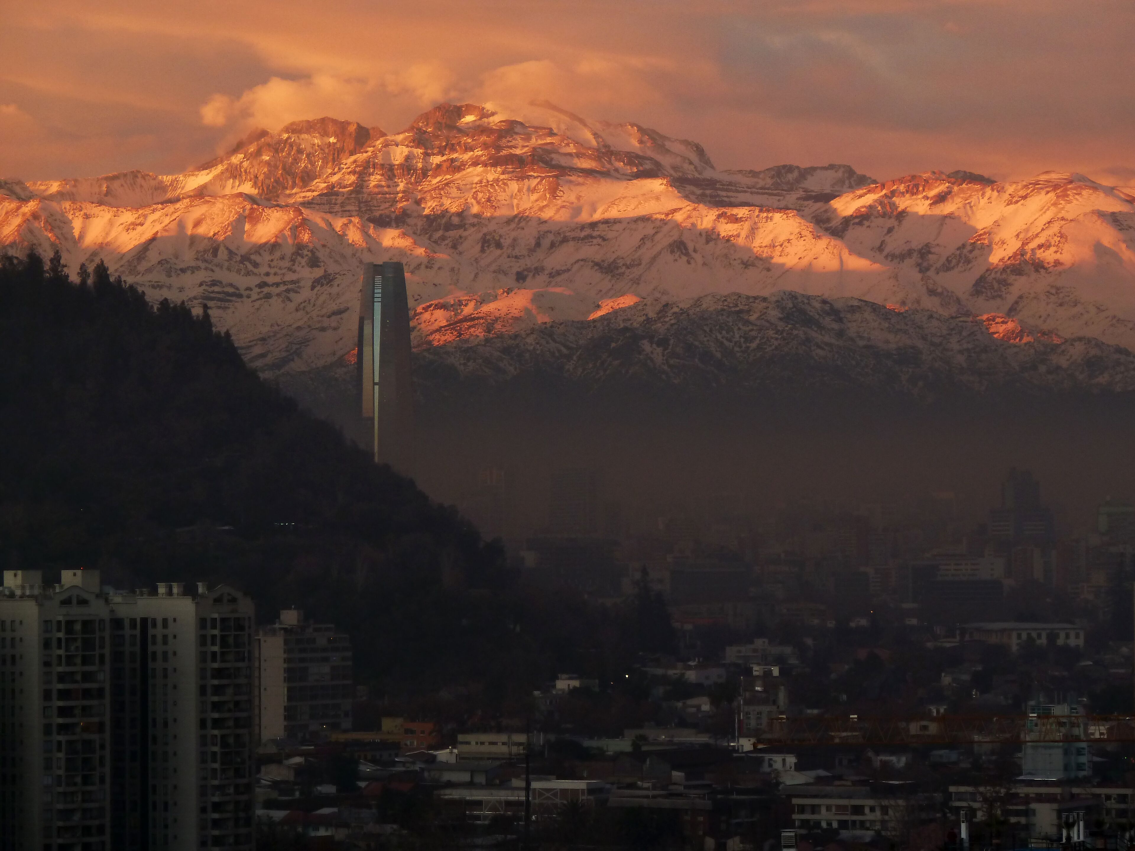 A cityscape with a prominent skyscraper in the foreground and a mountain range in the background.