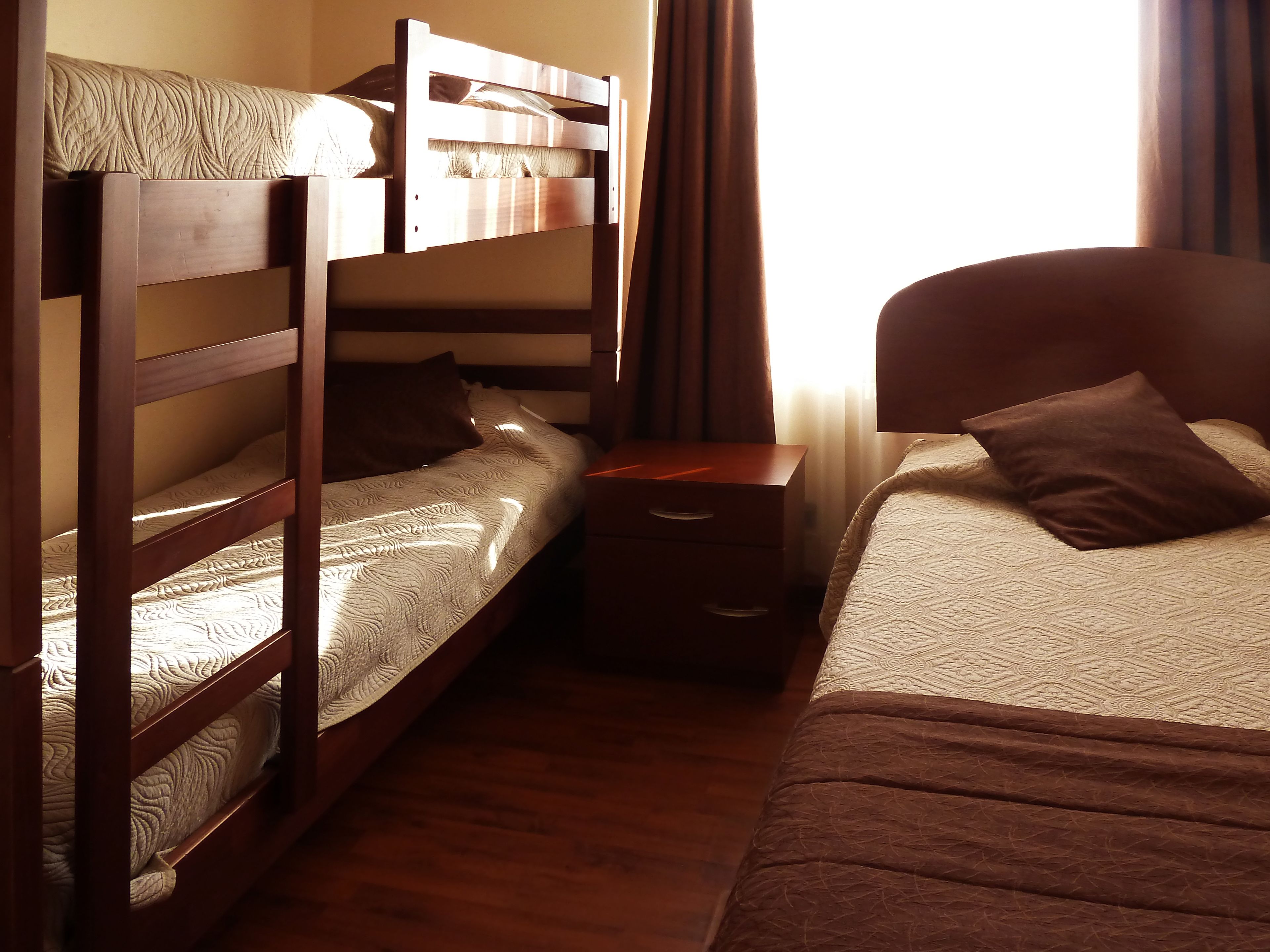 Una habitación con dos camas, una con cabecera y otra litera. Hay una mesita de noche entre las camas.