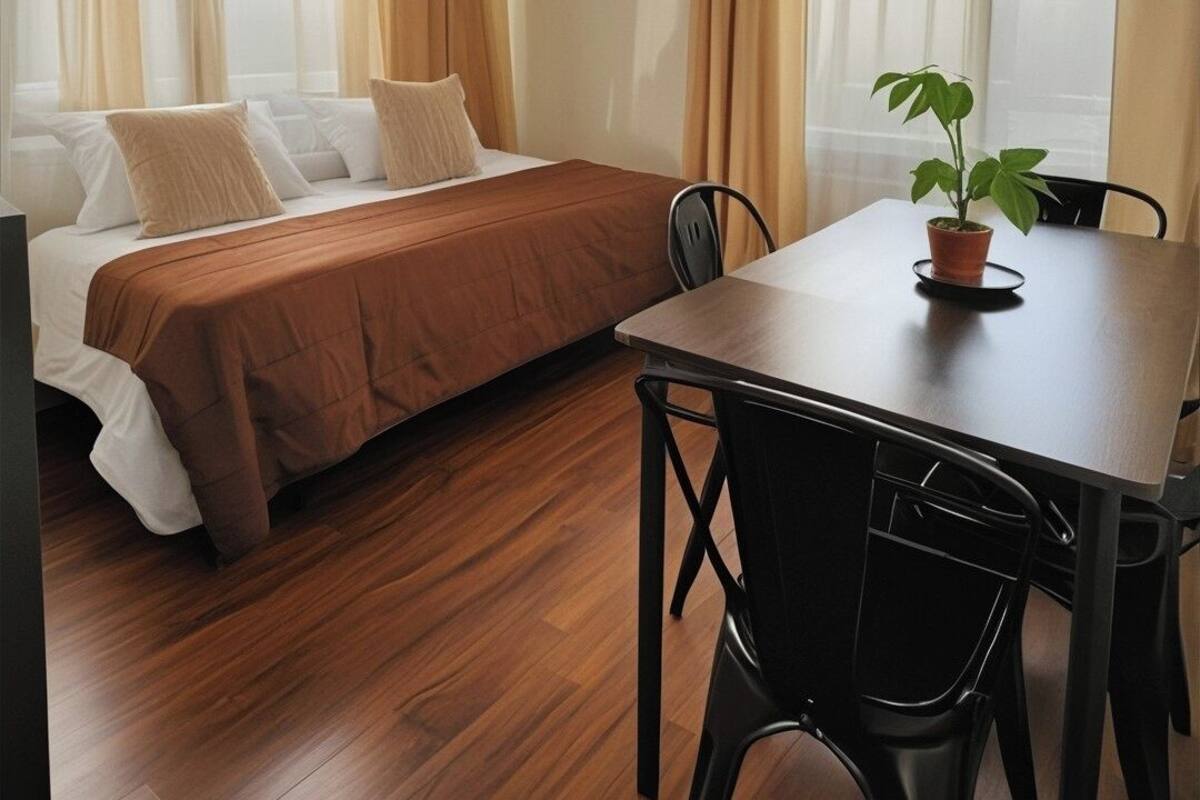 A room with a bed, a dining table, chairs, and a potted plant.