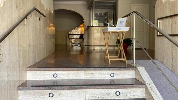 A staircase with a handrail, a small table with a sign, and a door in the background. - Hostal Comercio (Denia)