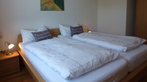 A double bed with white bedding and two pillows with text, a bedside lamp, and a painting on the wall. - Ferienwohnung Sauerlandblick (Korbach)